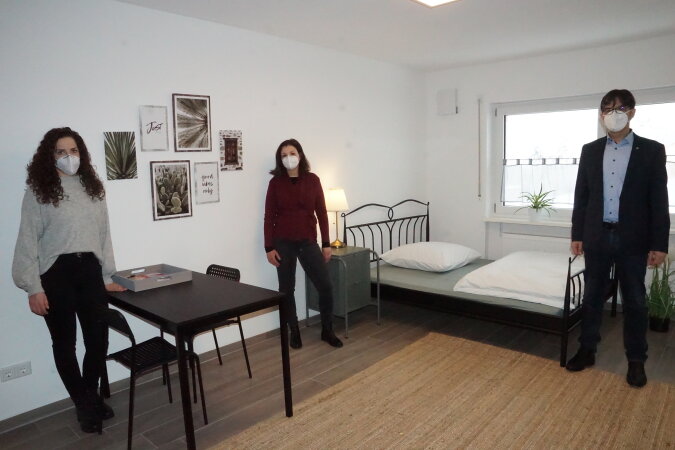 Drei Personen stehen in einem Ein-Zimmer-Apartment, 